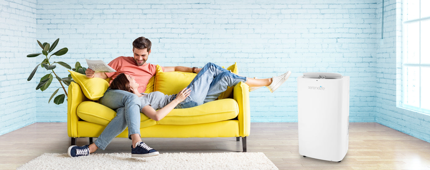 man and women sits on couch with serenelife branded air conditioner next to them