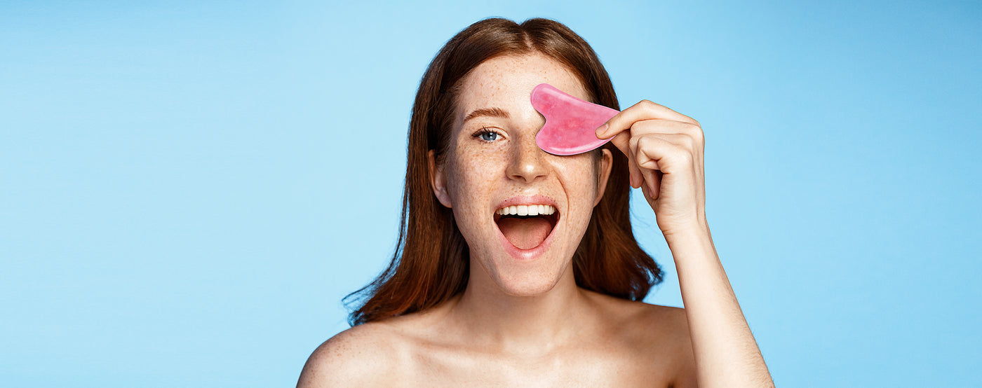 girl smiles and holds a Gua Sha over her eye