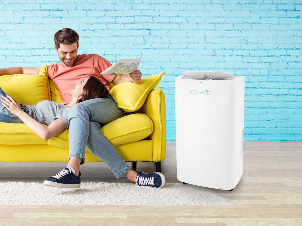 man and women sits on couch with serenelife branded air conditioner next to them